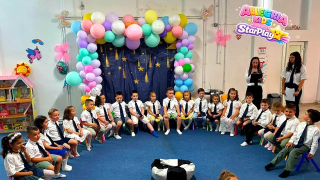 Copii la serbare în fața panoului cu baloane